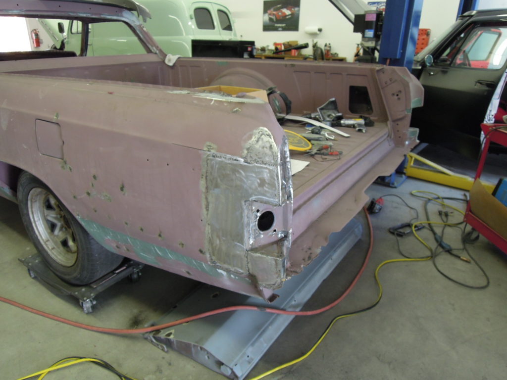 A pink car is being worked on in the shop.