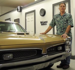 A man standing next to a car in a garage.